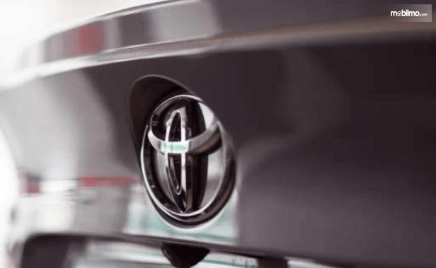 Gambar ini menunjukkan logo Toyota pada kendaraan dengan warna krom