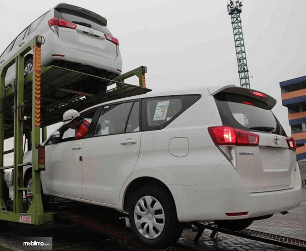 Gambar ini menunjukkan mobil Toyota warna putih sedang dinakkan ke kendaraan pengangkut