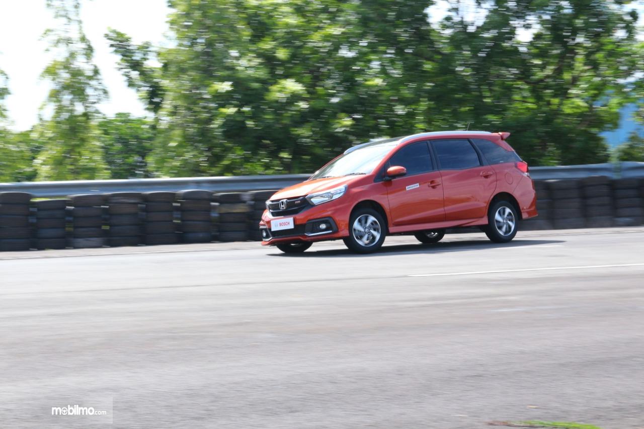 Gambar menunjukkan mobil Honda Mobilio RS CVT 2018 berwarna orange sedang berjalan di jalan Indonesia