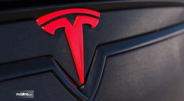 Gambar ini menunjukkan logo Tesla demhan warna merah
