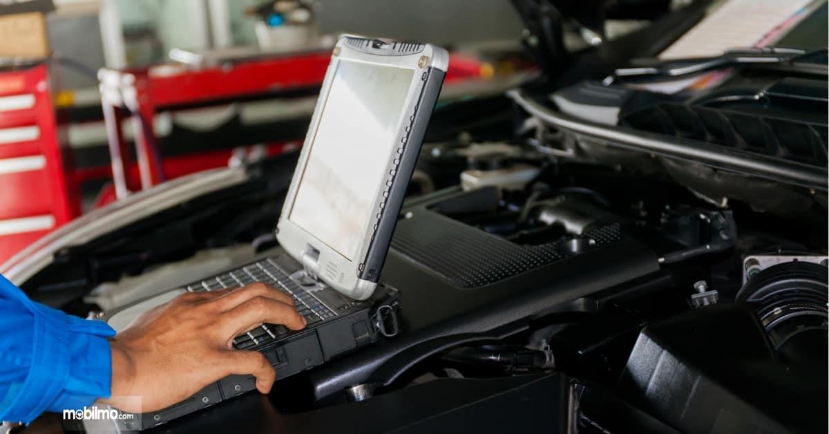 Foto seorang mekanik sedang melakukan diagnosa pada mobil menggunakan komputer
