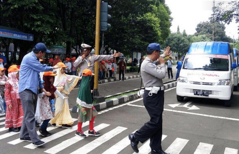Gambar ini menunjukkan beberapa polisi sedang menyebrangkan anak - anak