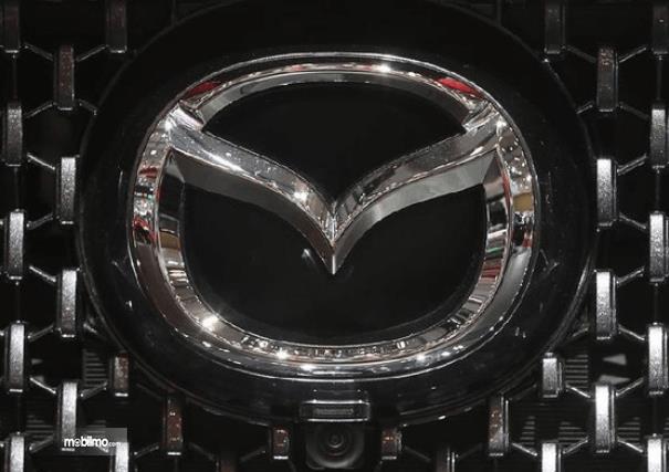 Gambar ini menunjukkan logo Mazda dengan aksen krom