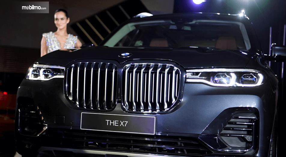 gambar ini menunjukkan mobil BMW X7 The President tampak depan dan ada seorang wanita sedang berdiri di sampingnya