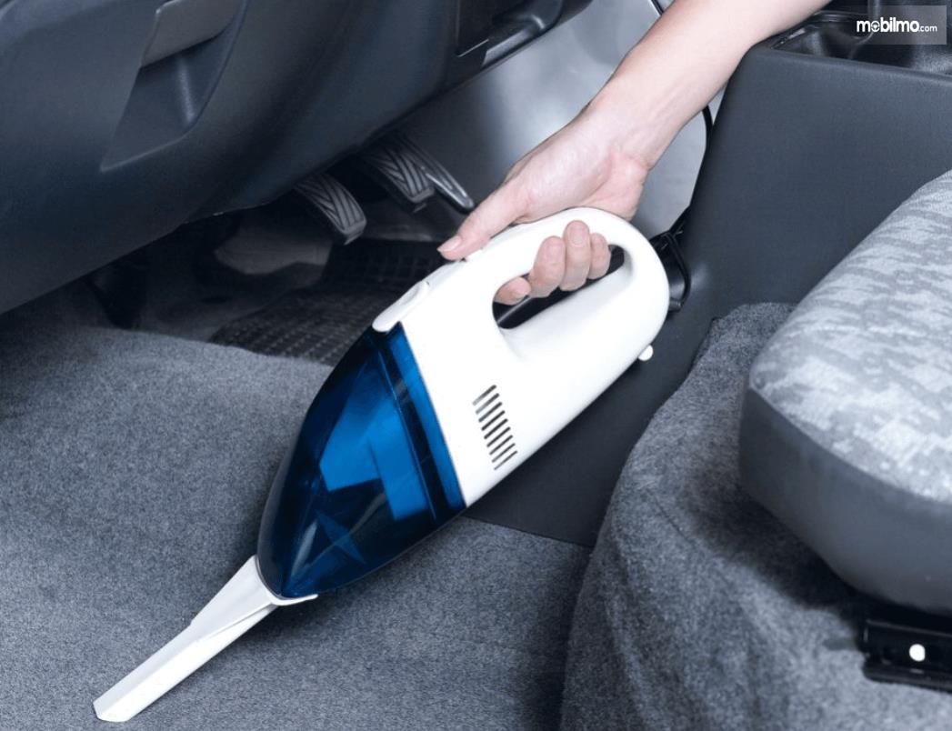 Gambar ini menunjukkan sebuah tangan memegang vacuum cleaner untuk menyedot kabin