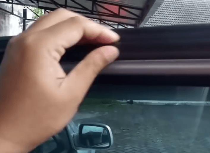 Gambar ini menunjukkan sebuah tangan memegang karet pada kaca mobil