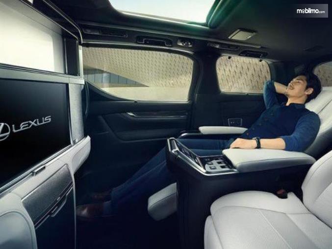 Gambar ini menunjukkan interior mobil Lexus LM300h dengan seorang pria sedang duduk