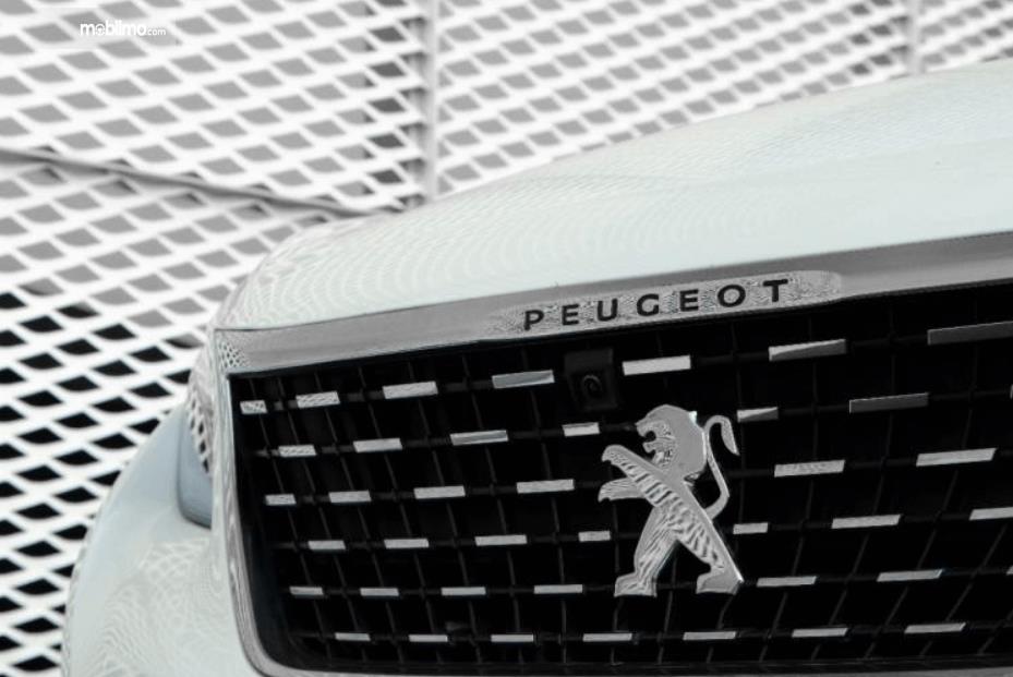 Gambar ini menunjukkan logo Peugeot pada mobil bagian depan