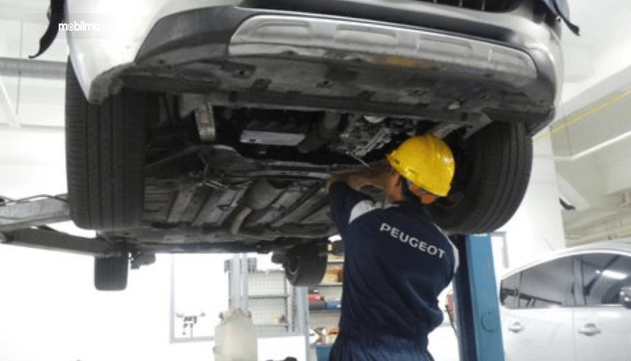 Gambar ini menunjukkan mekanik Peugeot memperbaiki mobil