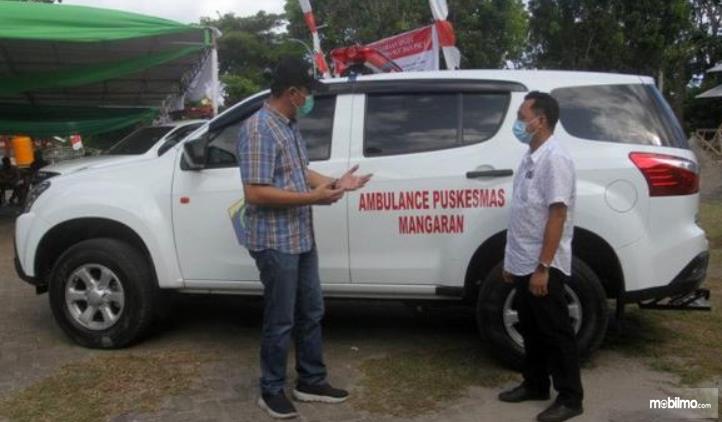 Gambar ini menunjukkan 2 orang berdiri disamping mobil Isuzu Mu-X Ambulans