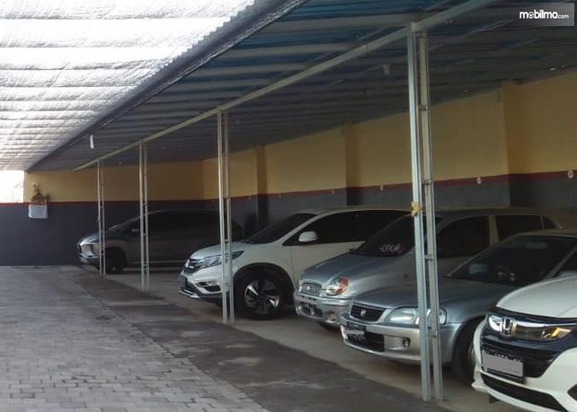 Gambar ini menunjukkan beberapa mobil berada di tempat parkir yang teduh
