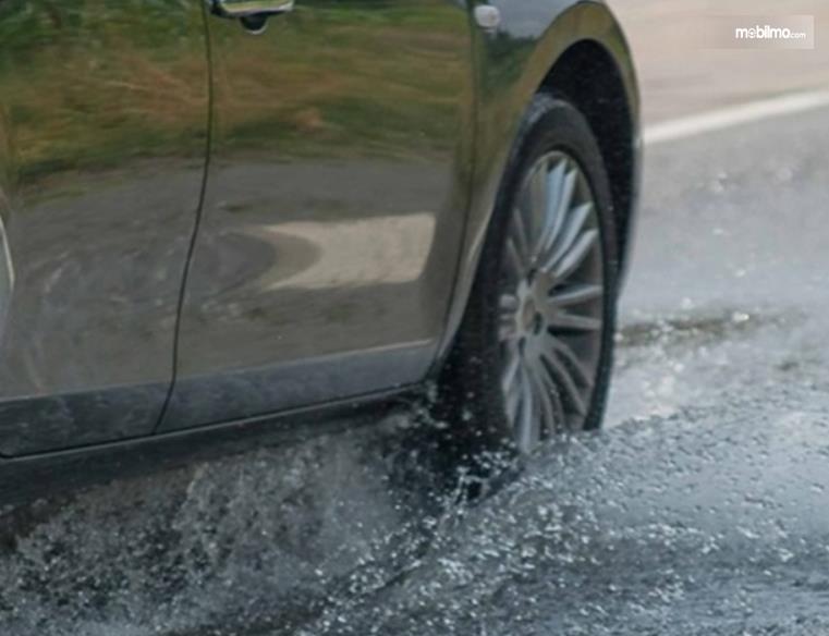 Gambar ini menunjukkan ban mobil sedang melintasi genangan air