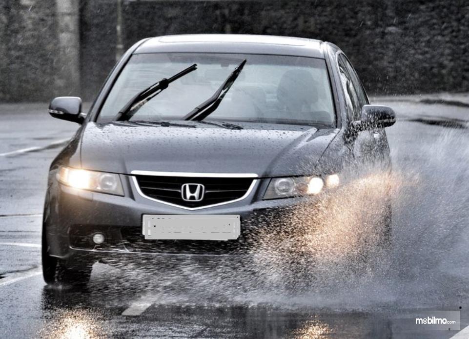Gambar ini menunjukkan sebuah mobil melintasi jalanan yang basah